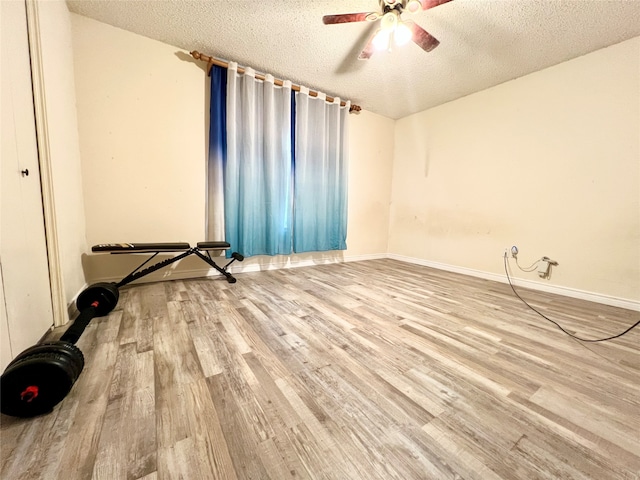 exercise room featuring light wood-type flooring, a textured ceiling, and ceiling fan