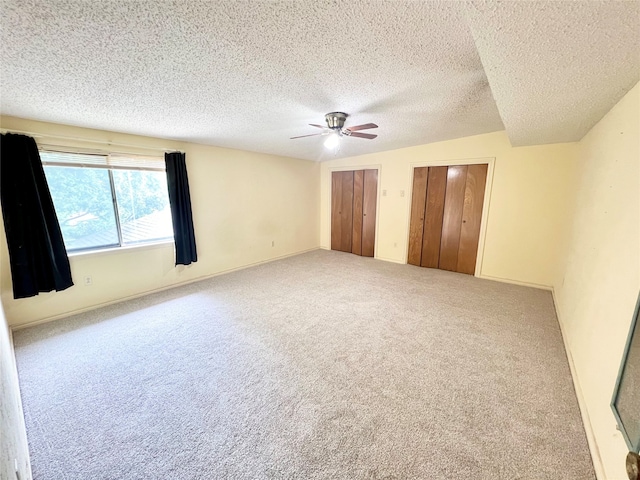 unfurnished bedroom with carpet flooring, ceiling fan, vaulted ceiling, a textured ceiling, and two closets