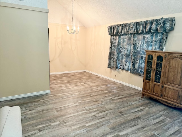 unfurnished dining area with wood-type flooring, vaulted ceiling, and an inviting chandelier