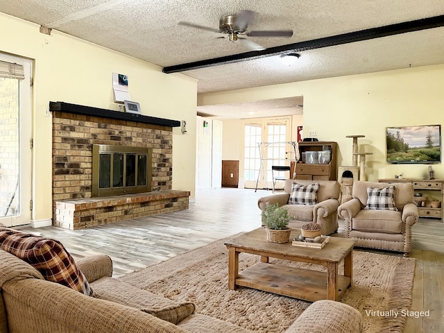 living room with a fireplace, ceiling fan, light hardwood / wood-style flooring, and a textured ceiling