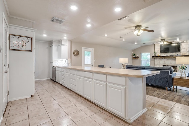 kitchen featuring a stone fireplace, white cabinets, stainless steel dishwasher, light tile patterned floors, and kitchen peninsula