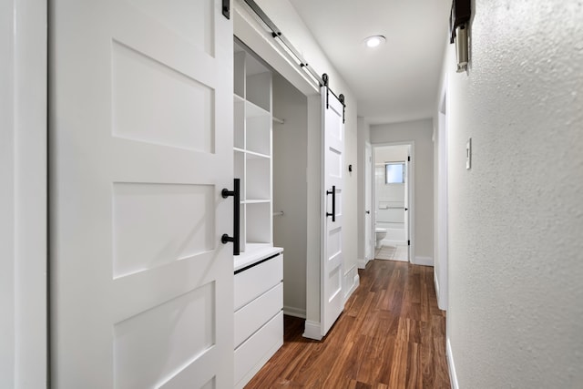 corridor with a barn door and dark hardwood / wood-style flooring