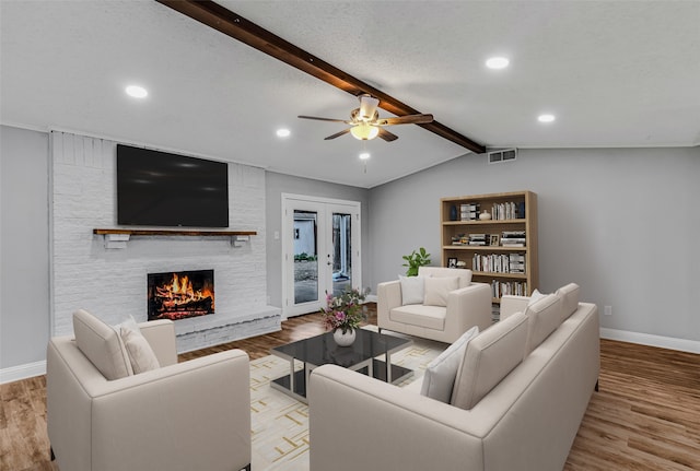 living room featuring ceiling fan, a large fireplace, light hardwood / wood-style flooring, and lofted ceiling with beams