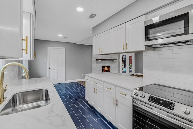 kitchen with white cabinetry, stainless steel appliances, tasteful backsplash, sink, and light stone counters