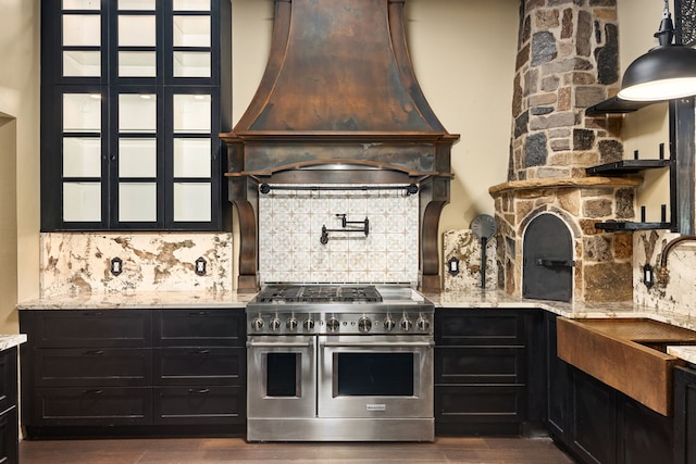 kitchen with custom range hood, light stone counters, tasteful backsplash, and range with two ovens