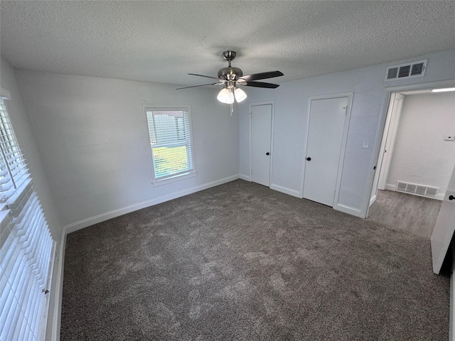 unfurnished bedroom featuring dark colored carpet, ceiling fan, and a textured ceiling