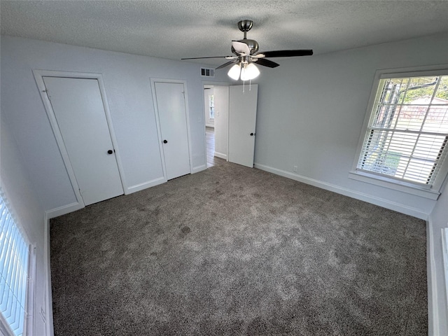 unfurnished bedroom with multiple closets, dark colored carpet, ceiling fan, and a textured ceiling