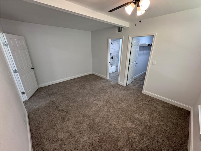 unfurnished bedroom with beamed ceiling, dark colored carpet, a walk in closet, ceiling fan, and a closet