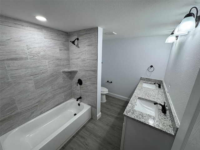 full bathroom featuring a textured ceiling, double vanity, tiled shower / bath combo, toilet, and hardwood / wood-style floors