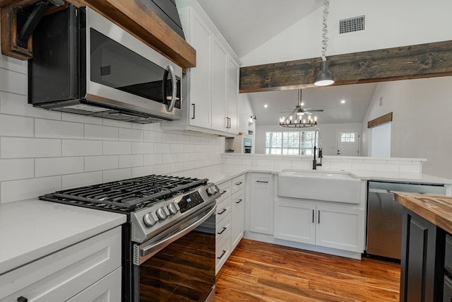 kitchen with vaulted ceiling with beams, stainless steel appliances, hanging light fixtures, sink, and light hardwood / wood-style floors