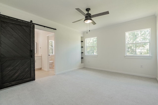 spare room featuring a barn door, light colored carpet, crown molding, and ceiling fan