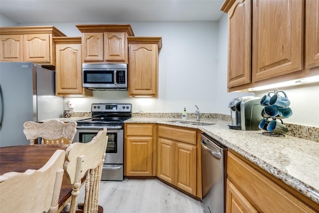 kitchen with sink, light hardwood / wood-style flooring, light stone countertops, and appliances with stainless steel finishes