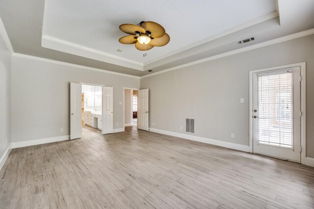 empty room with crown molding, light wood-type flooring, and a raised ceiling