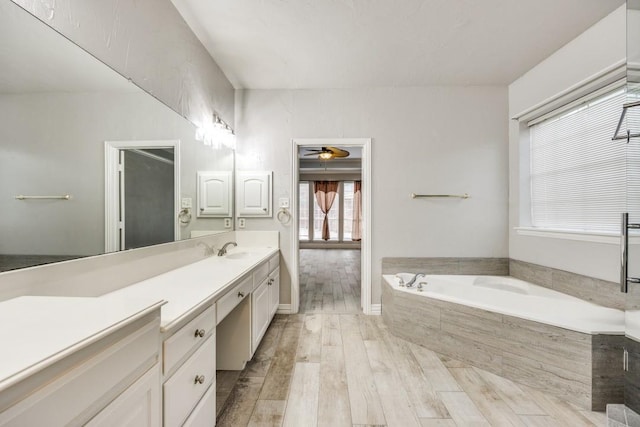 bathroom featuring ceiling fan, a relaxing tiled tub, hardwood / wood-style floors, and vanity