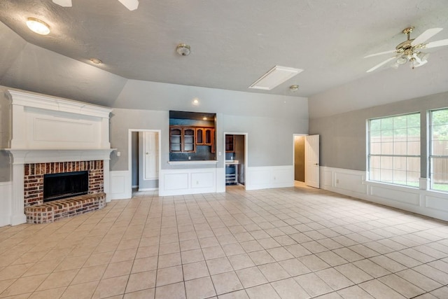 unfurnished living room with a textured ceiling, a brick fireplace, light tile patterned flooring, ceiling fan, and lofted ceiling with skylight