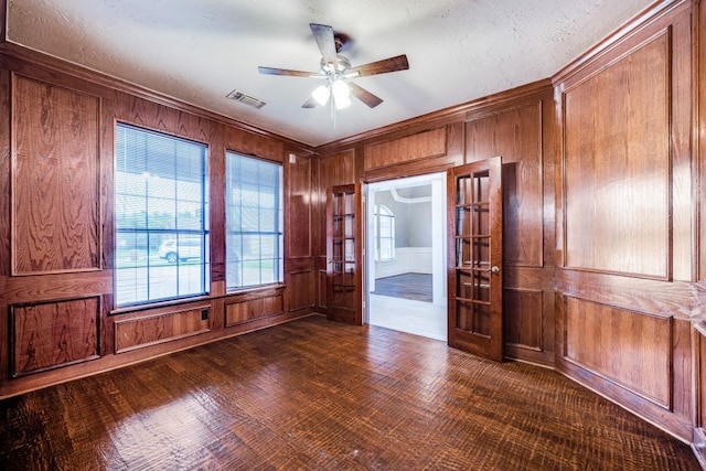 empty room with ornamental molding, ceiling fan, wooden walls, and a textured ceiling