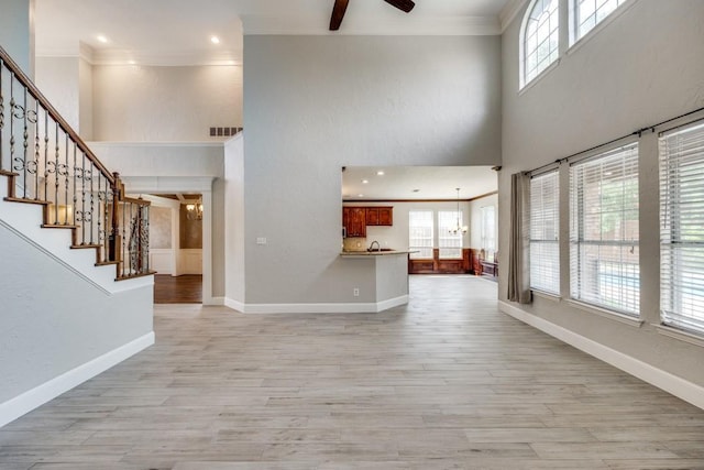 interior space with light hardwood / wood-style floors, a high ceiling, ornamental molding, and ceiling fan with notable chandelier