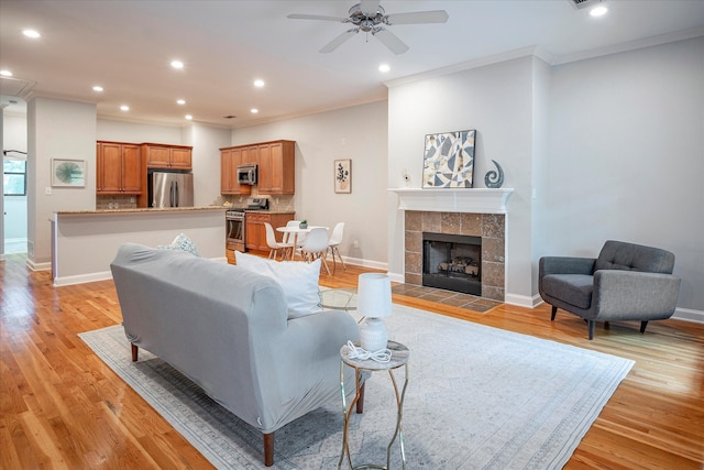 living room featuring a tile fireplace, crown molding, ceiling fan, and light hardwood / wood-style floors