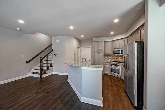 kitchen with appliances with stainless steel finishes, an island with sink, gray cabinetry, decorative backsplash, and light stone countertops