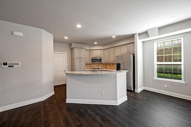 kitchen featuring dark wood-type flooring, light stone counters, stainless steel appliances, a kitchen island with sink, and backsplash