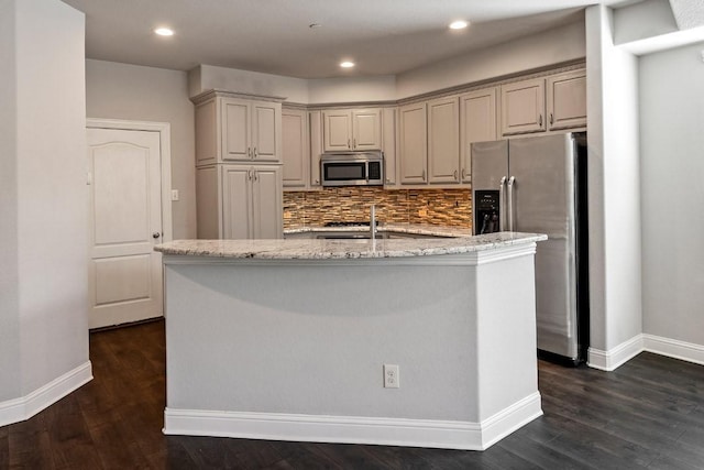 kitchen featuring an island with sink, appliances with stainless steel finishes, light stone counters, and decorative backsplash