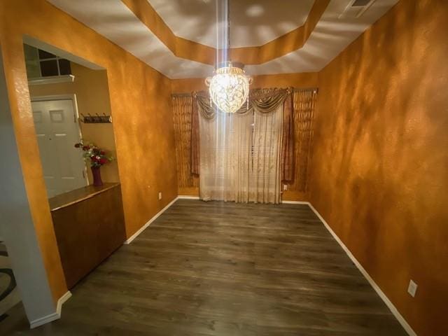 unfurnished dining area featuring a chandelier, dark wood-type flooring, and a tray ceiling