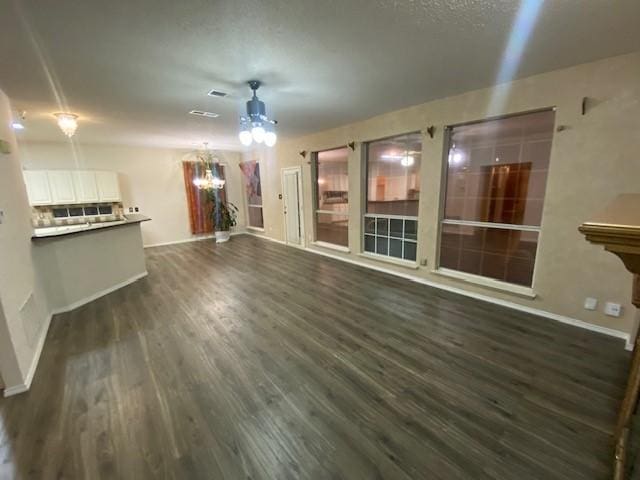 unfurnished living room with ceiling fan with notable chandelier and dark wood-type flooring