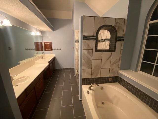 bathroom featuring tile patterned flooring, a relaxing tiled tub, vanity, and vaulted ceiling