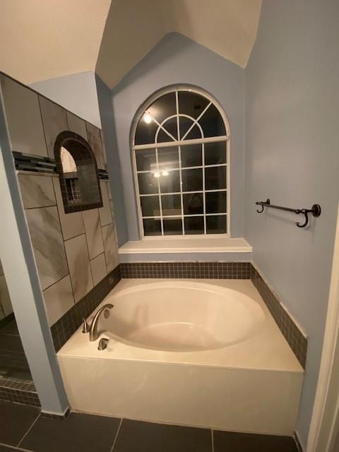 bathroom with tile patterned flooring, a washtub, and vaulted ceiling