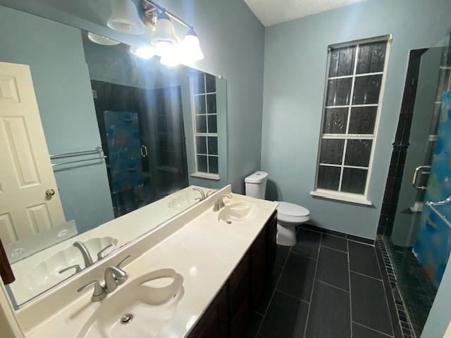 bathroom featuring tile patterned flooring, vanity, toilet, and a shower with door