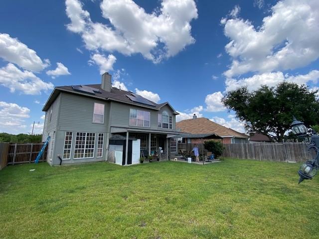 back of property with a yard, a patio, and solar panels