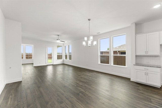 unfurnished living room with ceiling fan with notable chandelier, plenty of natural light, and dark hardwood / wood-style flooring