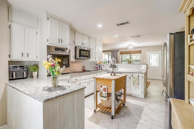 kitchen featuring stainless steel appliances, a center island, light stone counters, light tile patterned floors, and backsplash