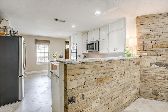 kitchen featuring light stone countertops, appliances with stainless steel finishes, a peninsula, visible vents, and white cabinets
