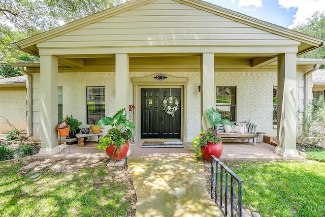 view of exterior entry with covered porch and brick siding