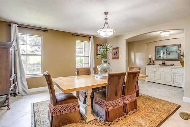 dining area with arched walkways, a wealth of natural light, baseboards, and light tile patterned flooring