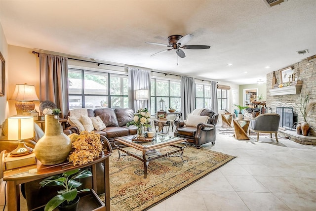 living room with a textured ceiling, a fireplace, ceiling fan, and a healthy amount of sunlight