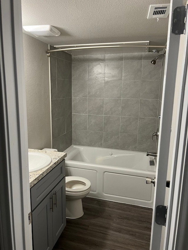 full bathroom with vanity, wood-type flooring, tiled shower / bath combo, toilet, and a textured ceiling