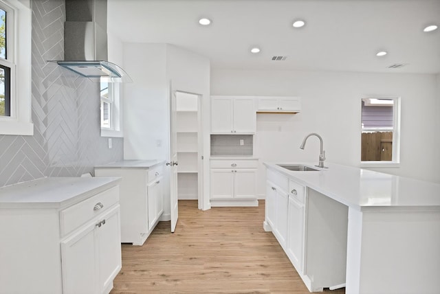 kitchen with white cabinets, decorative backsplash, sink, a center island with sink, and light hardwood / wood-style flooring