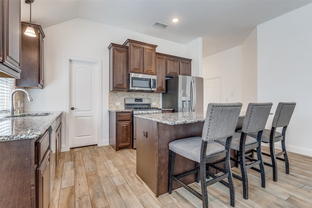 kitchen with sink, a center island, appliances with stainless steel finishes, light hardwood / wood-style flooring, and tasteful backsplash