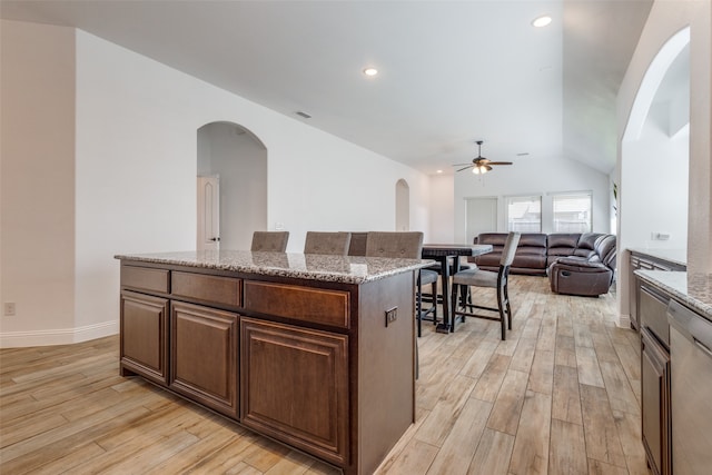 kitchen featuring light wood-type flooring, light stone counters, vaulted ceiling, a kitchen island, and ceiling fan