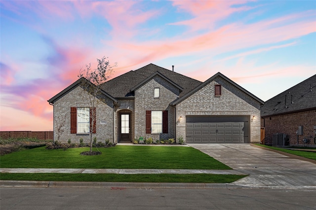 french country home featuring a garage, central AC unit, and a lawn