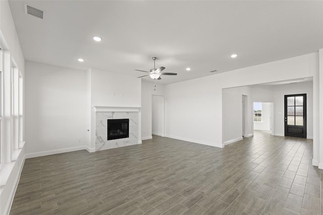 unfurnished living room featuring a premium fireplace, dark wood-type flooring, and ceiling fan