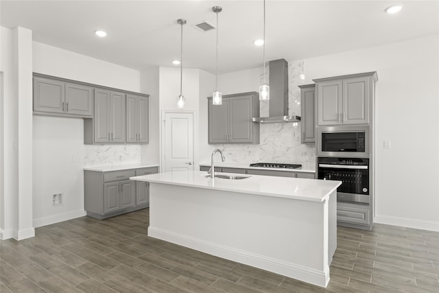 kitchen with stainless steel appliances, a center island with sink, sink, dark hardwood / wood-style floors, and wall chimney range hood