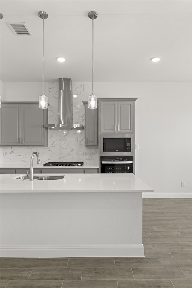 kitchen featuring appliances with stainless steel finishes, gray cabinets, wall chimney exhaust hood, and decorative light fixtures