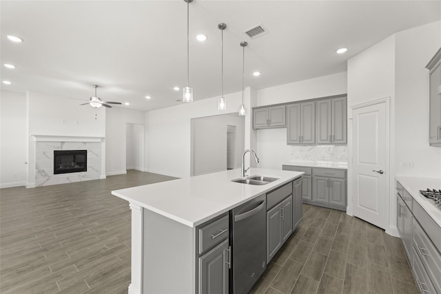 kitchen featuring dishwasher, a high end fireplace, a center island with sink, and gray cabinets