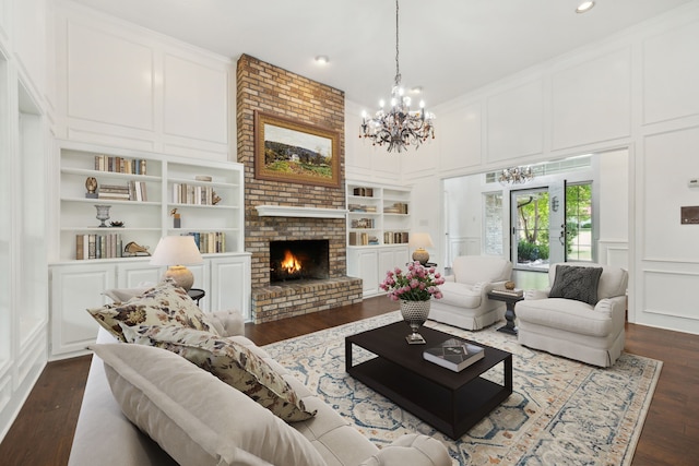 living room featuring built in features, a fireplace, brick wall, dark wood-type flooring, and a notable chandelier