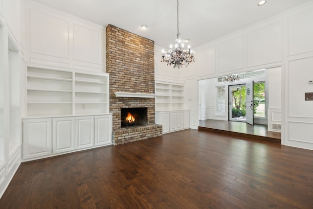 unfurnished living room featuring built in shelves, dark hardwood / wood-style floors, ornamental molding, a notable chandelier, and a brick fireplace