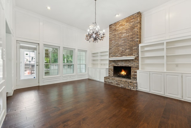 unfurnished living room featuring built in features, an inviting chandelier, dark hardwood / wood-style floors, a brick fireplace, and brick wall