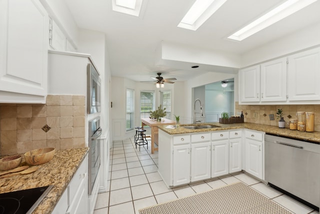 kitchen with appliances with stainless steel finishes, sink, kitchen peninsula, light tile patterned flooring, and ceiling fan